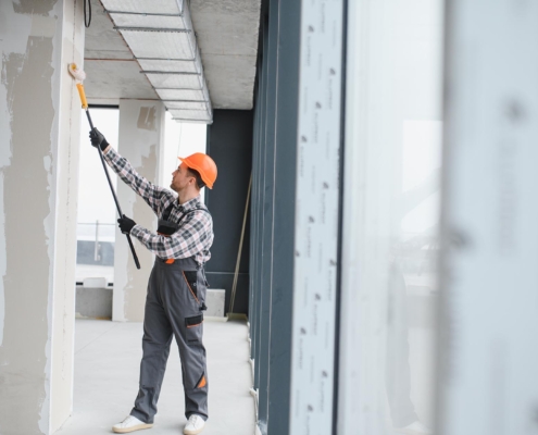 Construction Worker Painting Walls With Roller In Building Renovation